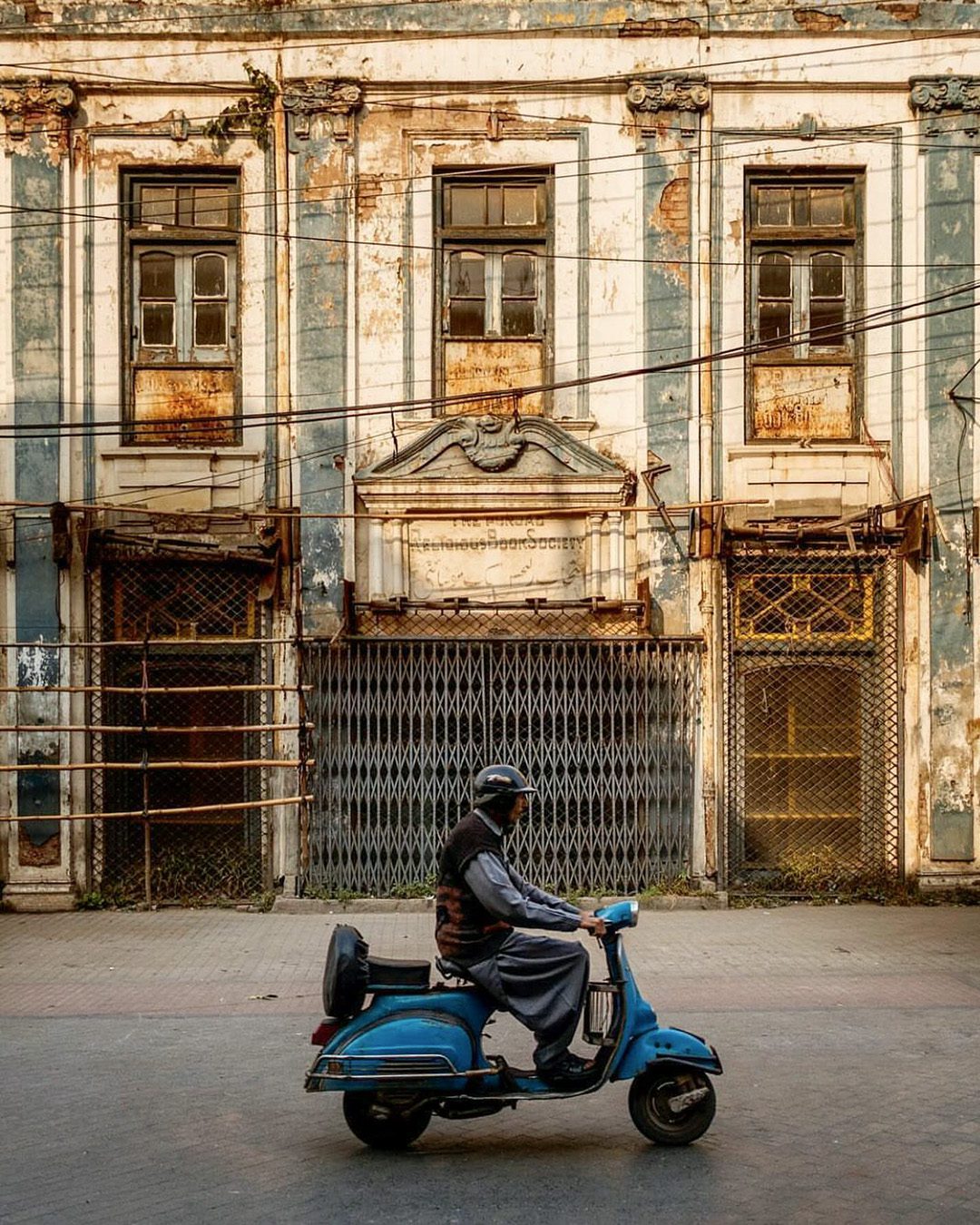 A photograph by Fakhar-e-Alam Bhatti featuring a vespa scooter going past along the Anarkali Bazaar in Lahore. Background features the Punjab Religion Book Society Building.