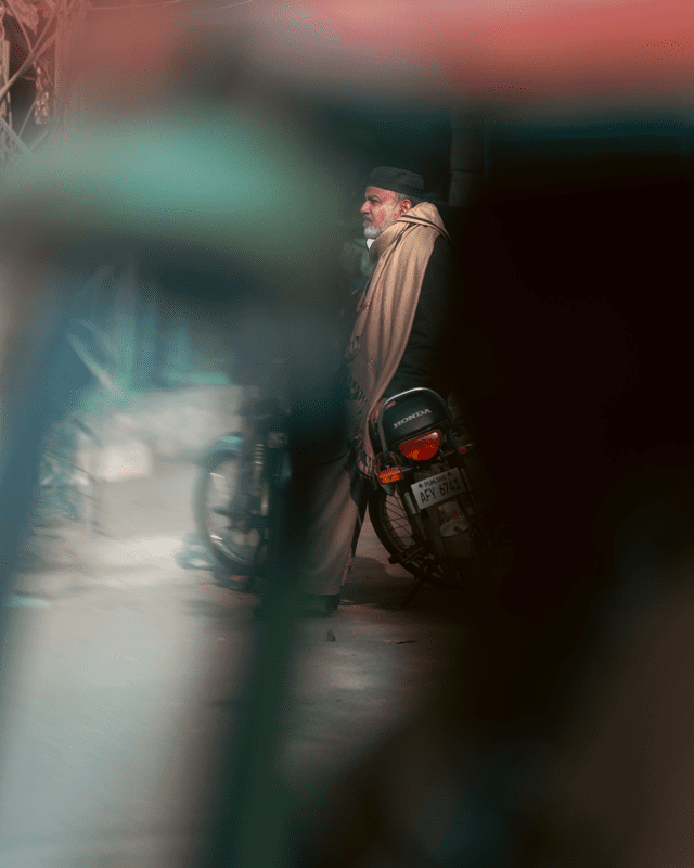 A telephoto shot of a man sitting on a bike wiht a rickshaw passing by. The longer focal length and f/1.8 aperture blurs the foreground completely.