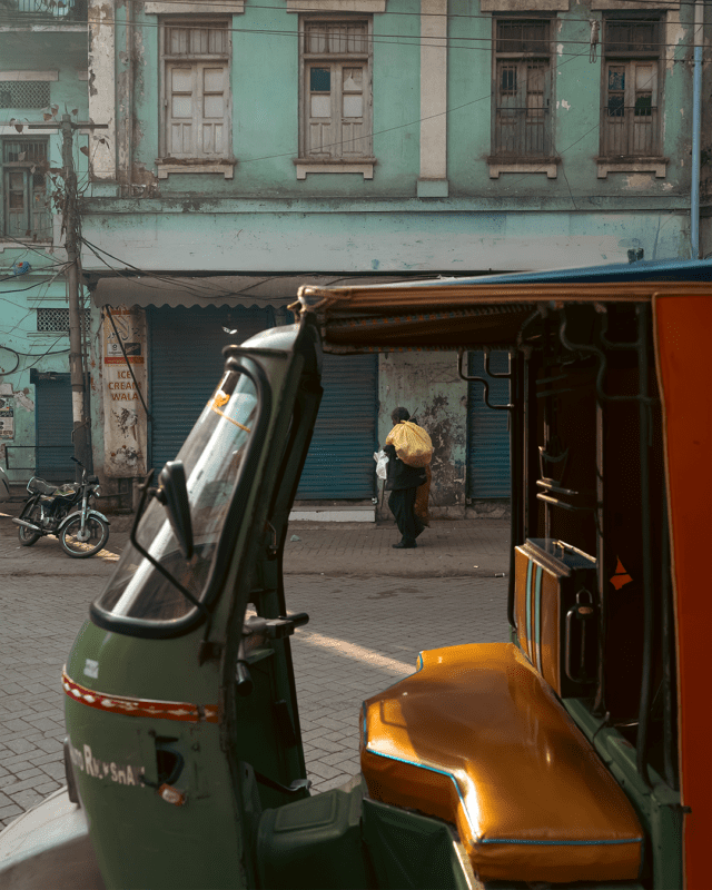 A man walking with a yellow bag appear through the opening of a rickshaw parked on a street in old Lahore